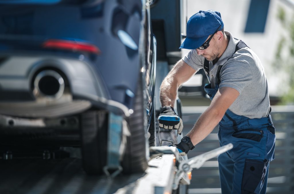 man securing car onto back of tow truck